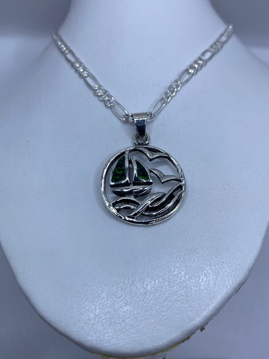 Primer plano del dije de plata mostrando el relieve del velero y la vela con ópalo