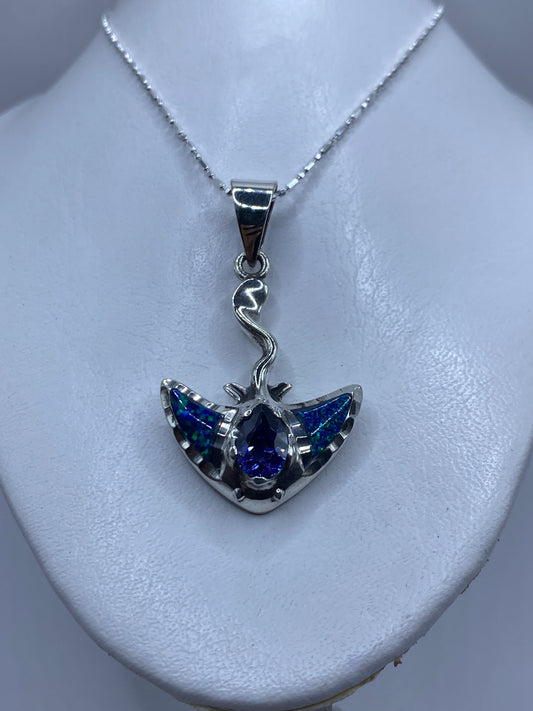 Detalle lateral del dije mostrando el engaste delicado de la piedra azul y las alas de plata