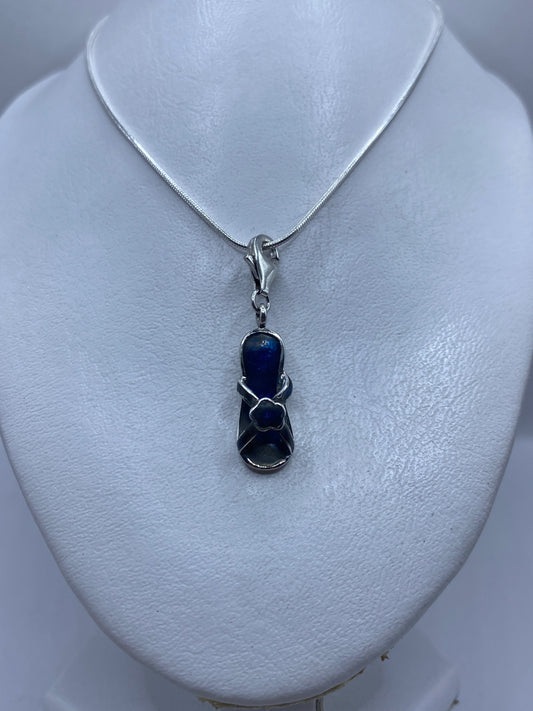 Dije de 4.1 cm de largo con piedra azul en primer plano sobre pecho de mujer