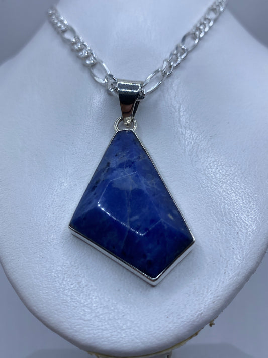Detalle frontal del dije mostrando la piedra azul y el engaste a mano