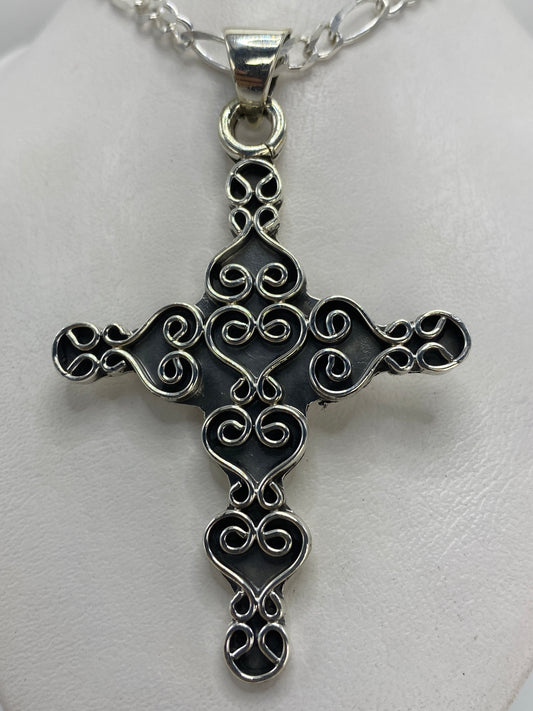 Vista frontal del dije cruz de 6.8 cm mostrando el diseño ornamentado con corazones