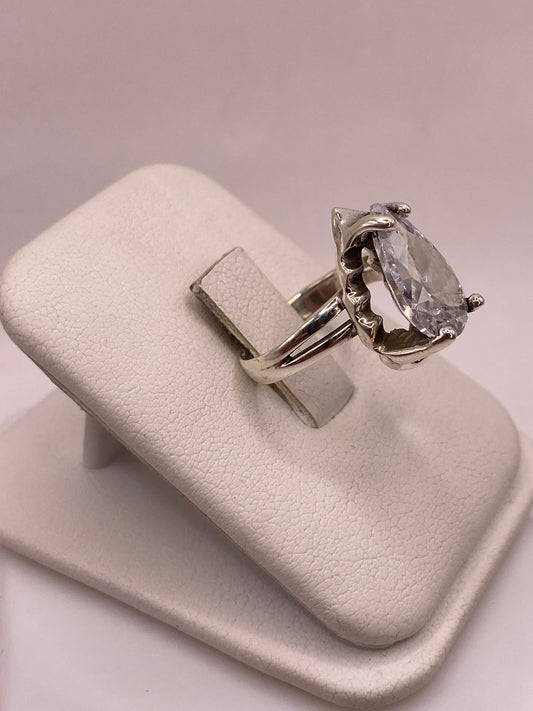 Vista lateral del anillo solitario en plata con montura calada y circonia pera sobre soporte blanco