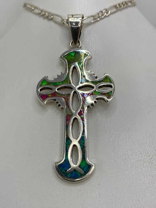 Vista frontal del dije cruz religioso de plata 925 con ópalo multicolor y alas ornamentales
