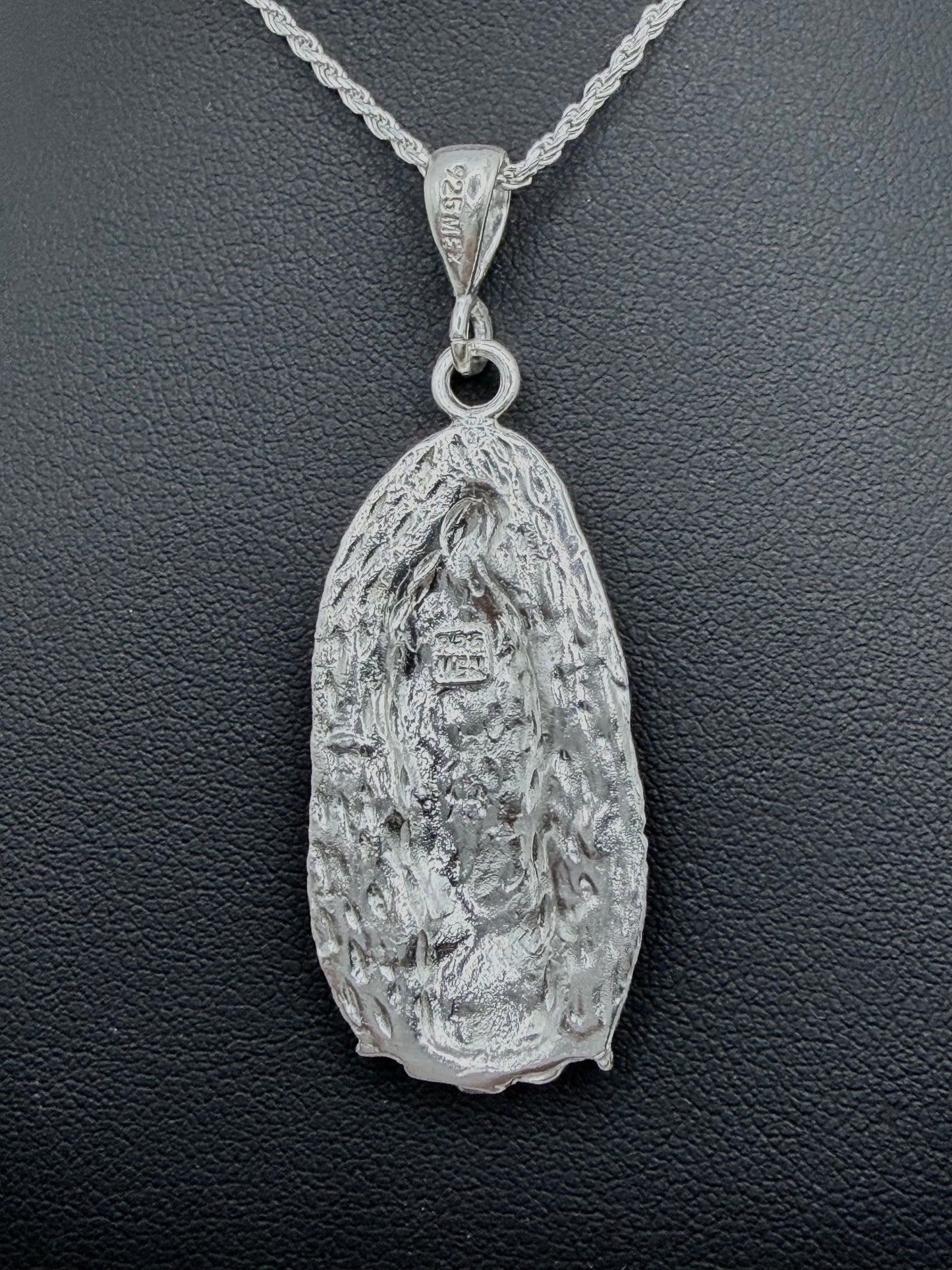 Detalle frontal del dije Virgen Guadalupe repujado con profundidad artesanal, relieve tallado en plata pura