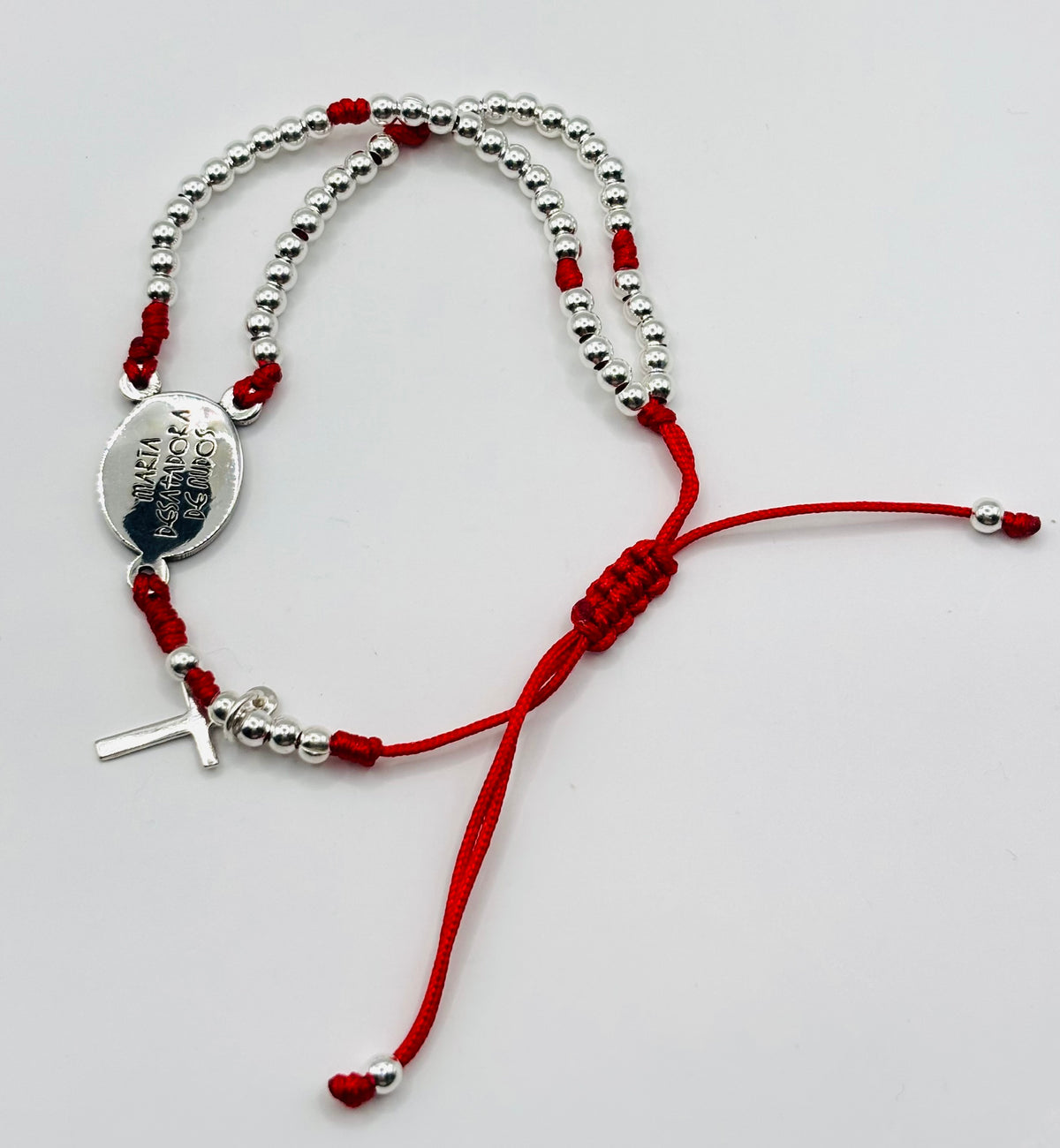 Detalle de la medalla de la Virgen Desatanudos en plata fundida, con cuentas plateadas y hilo rojo tejido