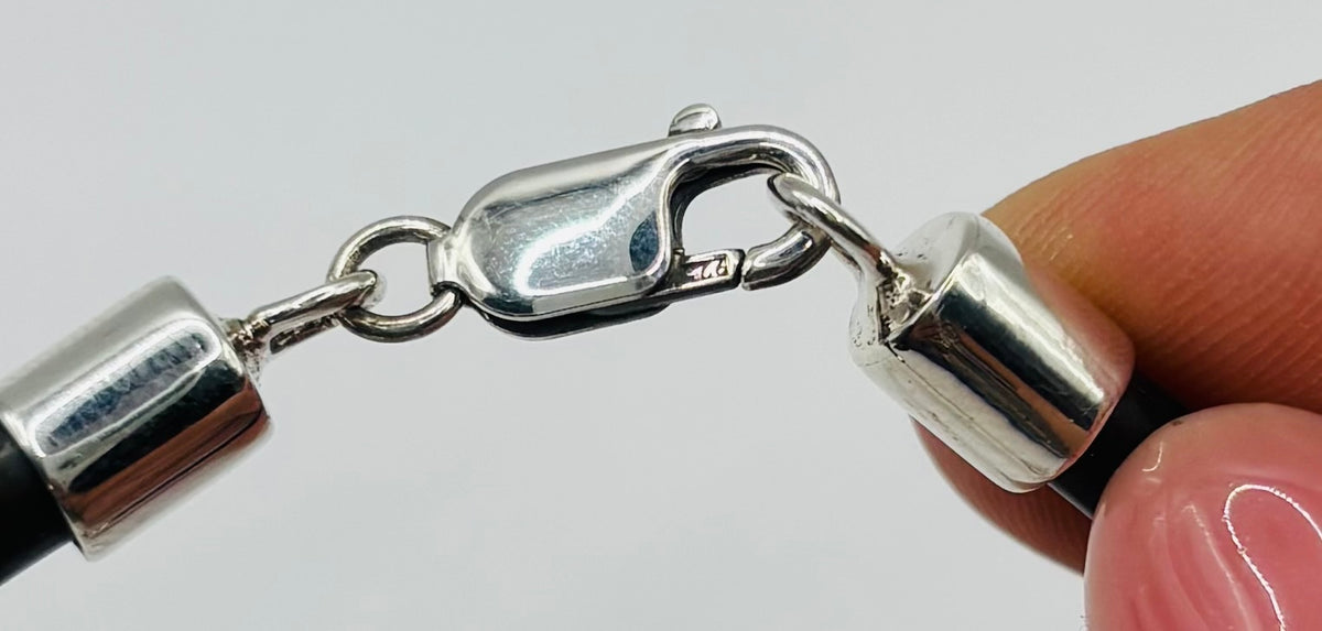 Pulsera de caucho negro con crucifijo de plata, vista lateral sobre muñeca