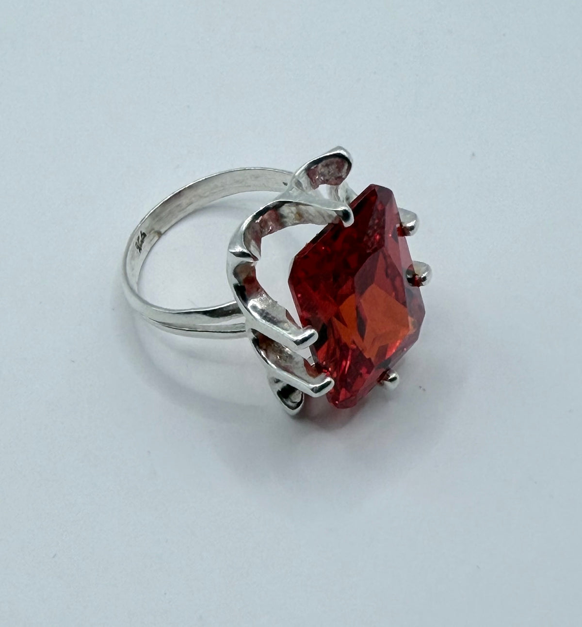 Vista frontal del anillo con la circonia roja brillante bajo luz natural, demostrando el corte facetado