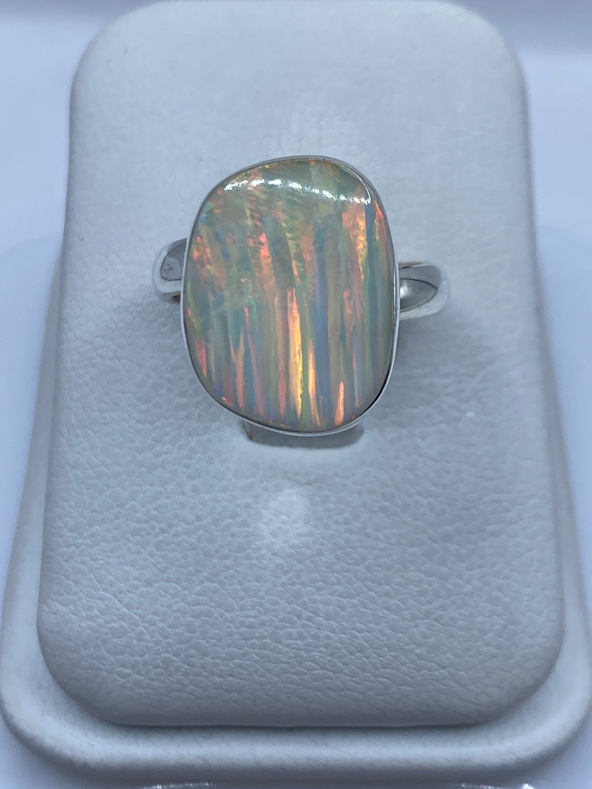 Anillo de plata con ópalo de fuego multicolor en mano de mujer, mostrando reflejos rojo-naranja