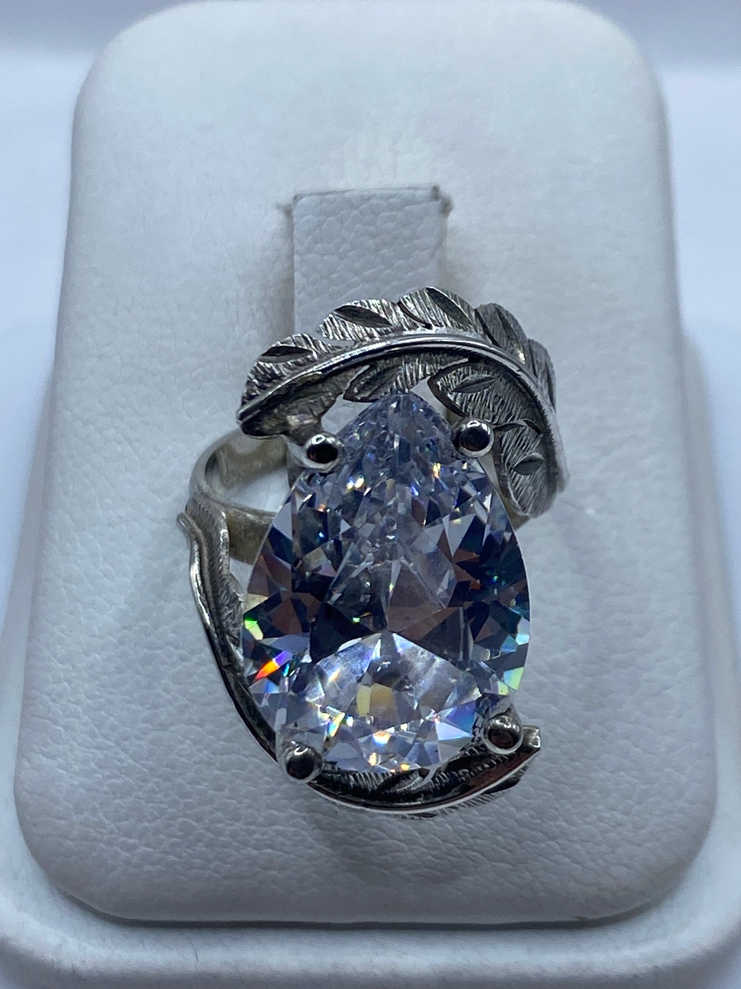 Anillo de plata solitario con circonia blanca sobre almohada blanca, vista frontal mostrando el fuego de la piedra