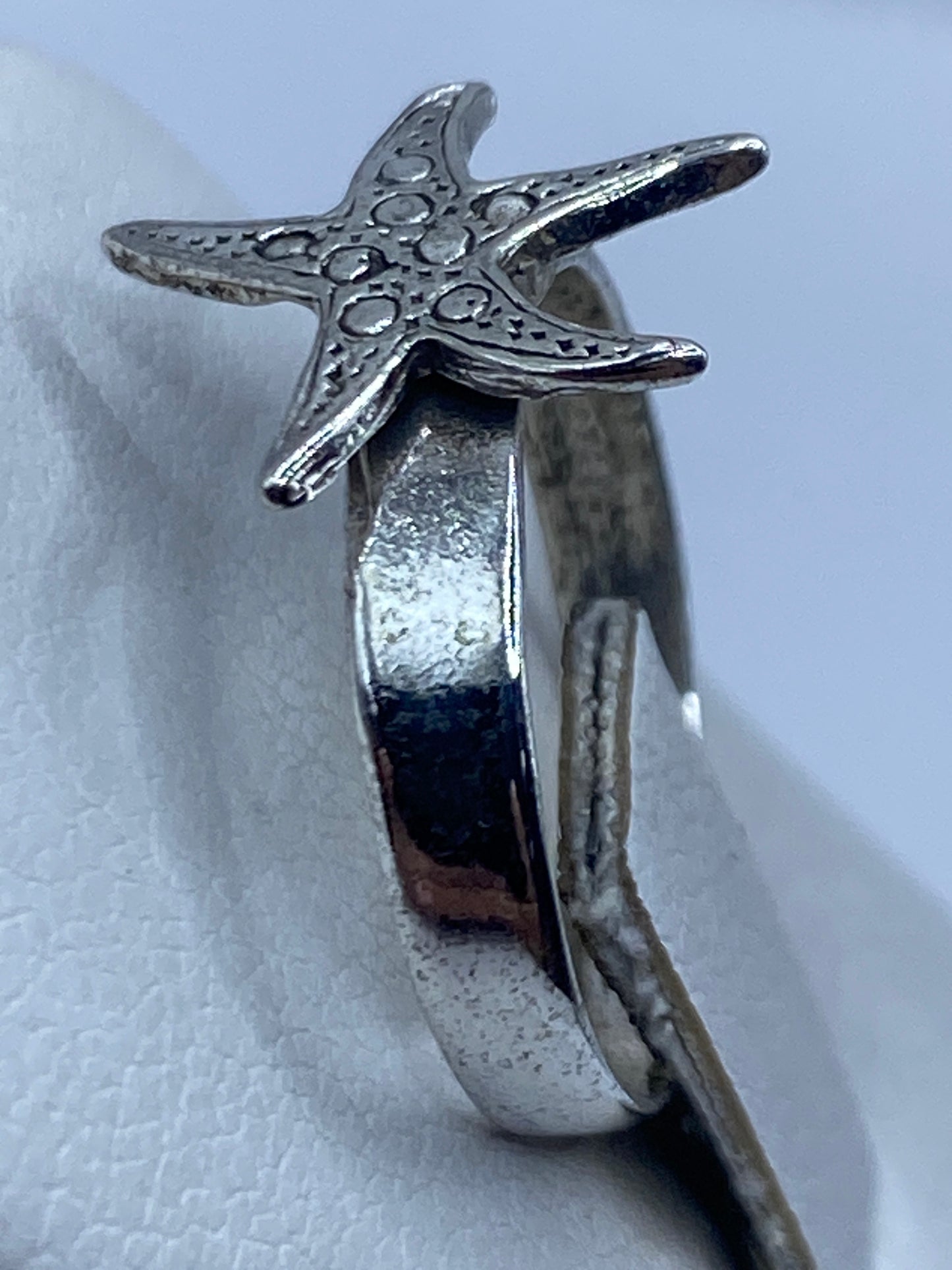 Anillo de plata estrella marina puesto en la mano con textura marina visible