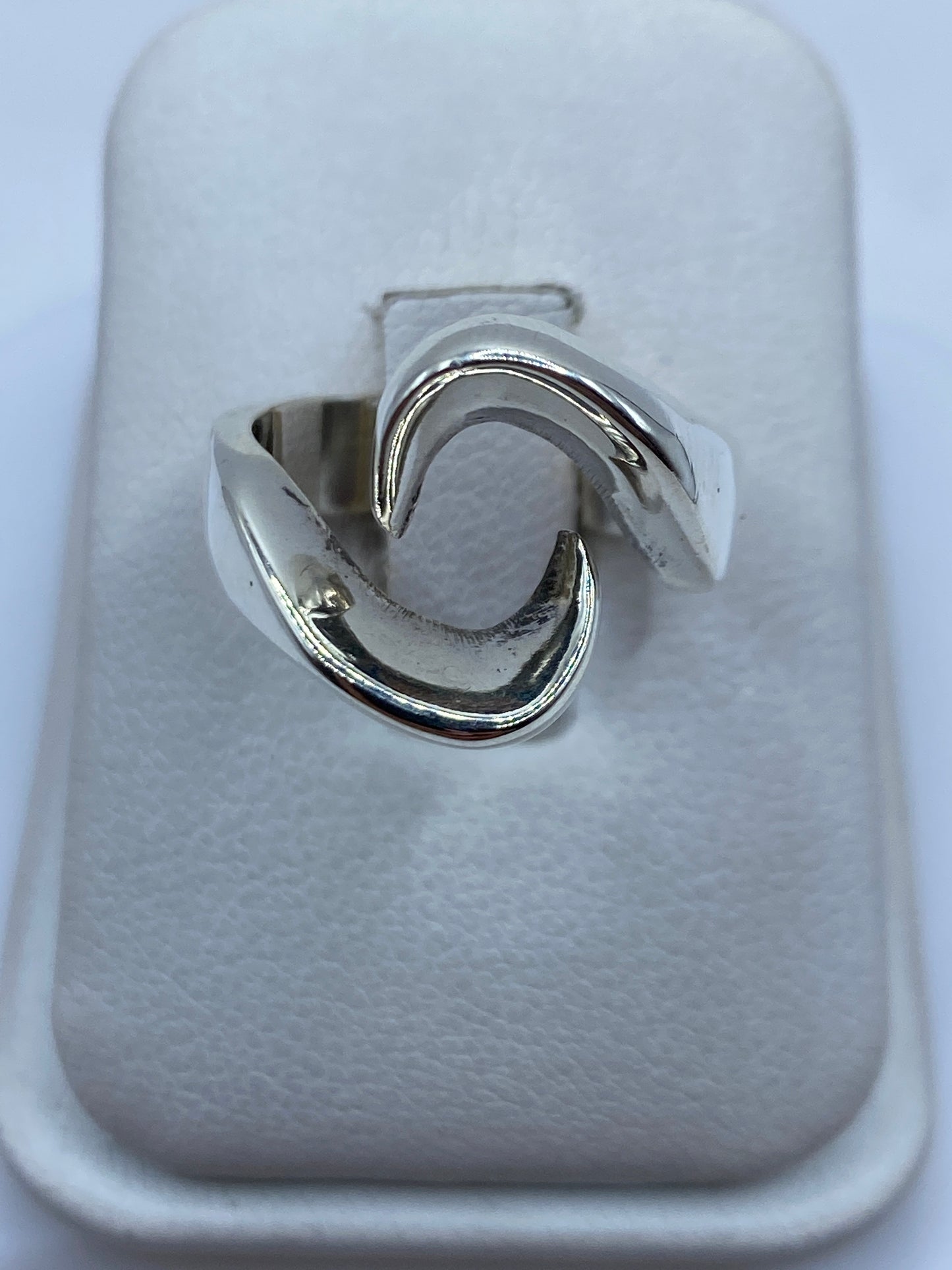 Anillo de plata con formas fluidas ondulantes, vista frontal sobre la mano de una mujer