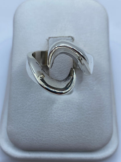 Anillo de plata con formas fluidas ondulantes, vista frontal sobre la mano de una mujer