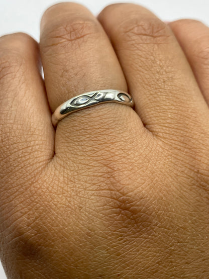 Anillo de plata pulida sobre fondo gris, vista lateral mostrando el acabado perfecto