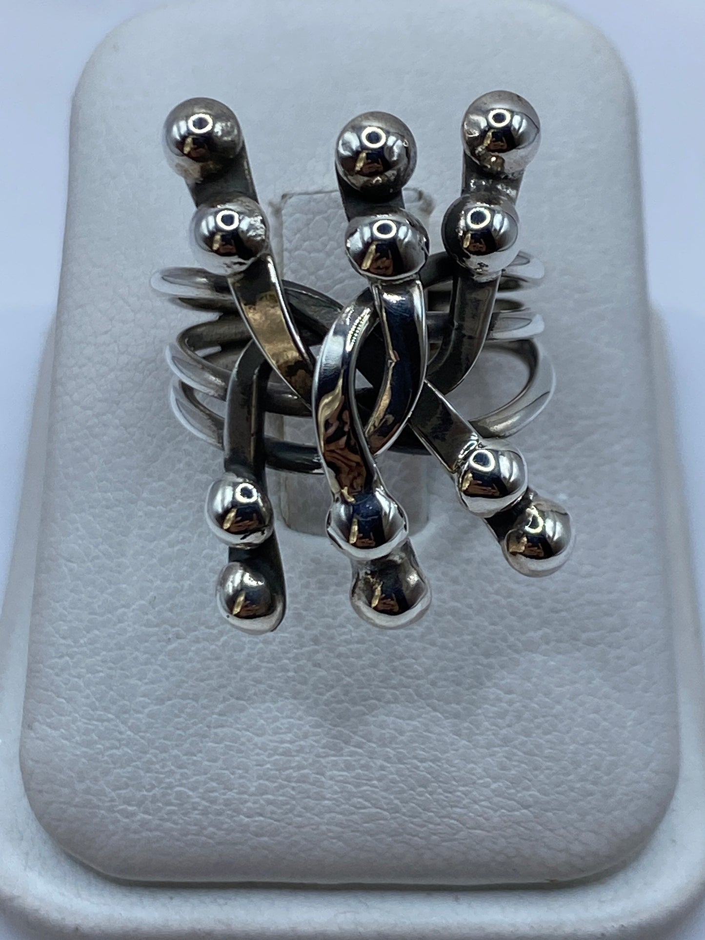 Anillo minimalista de plata con tres esferas suspendidas en banda triple, vista frontal sobre fondo blanco