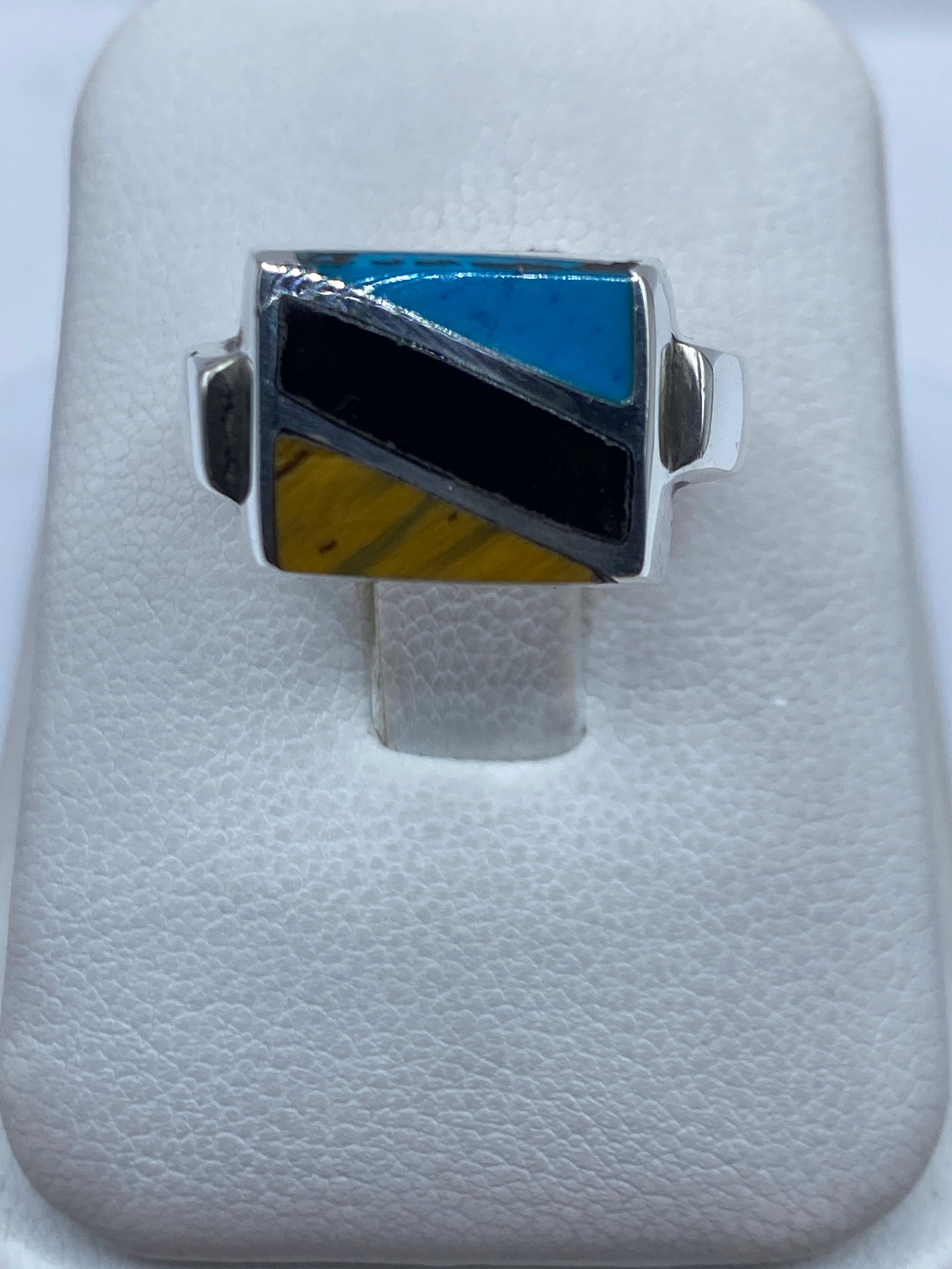 Anillo de plata con turquesa azul cielo en diseño geométrico, visto desde arriba sobre tela blanca