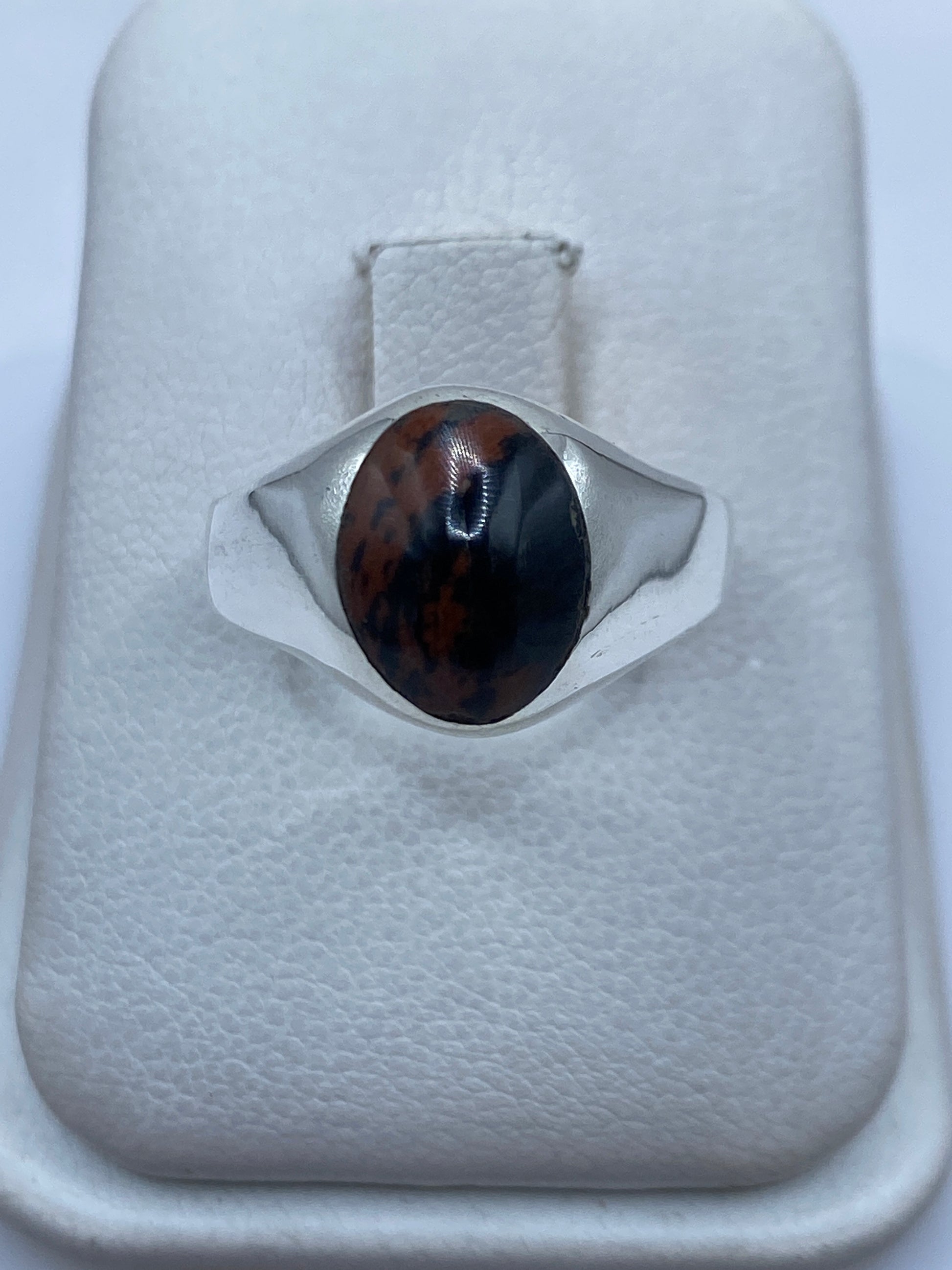 Anillo de plata solitario minimalista con piedra negra y marrón en la mano de una persona