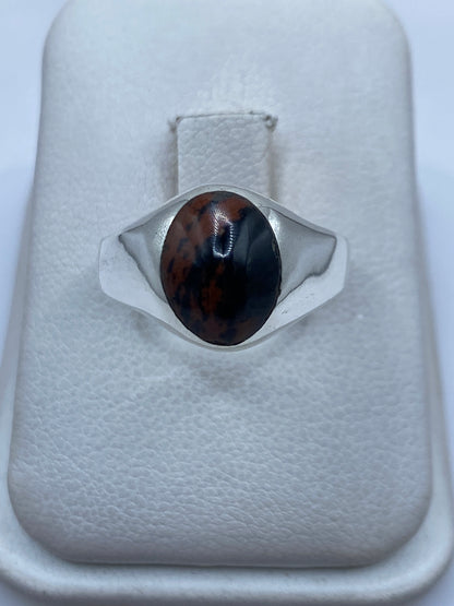 Anillo de plata solitario minimalista con piedra negra y marrón en la mano de una persona