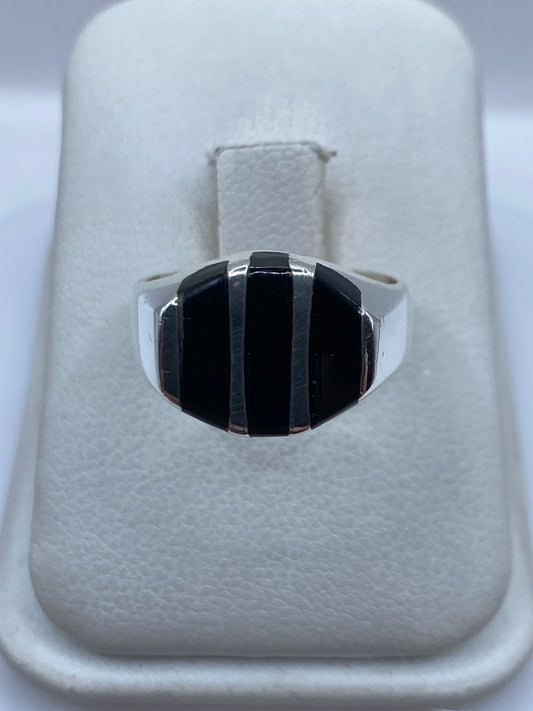 Anillo de plata con ónix negro en franjas escalonadas, vista frontal sobre estuche blanco
