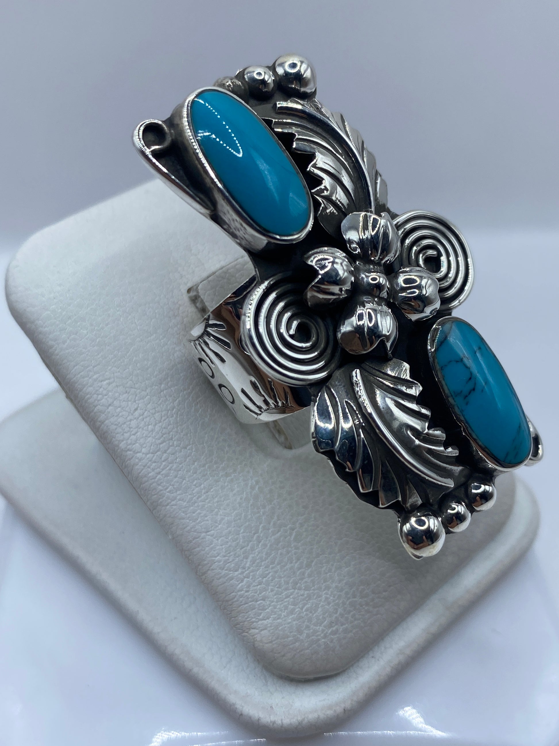Detalle lateral del anillo mostrando el engaste de turquesa a mano y la textura repujada de la plata