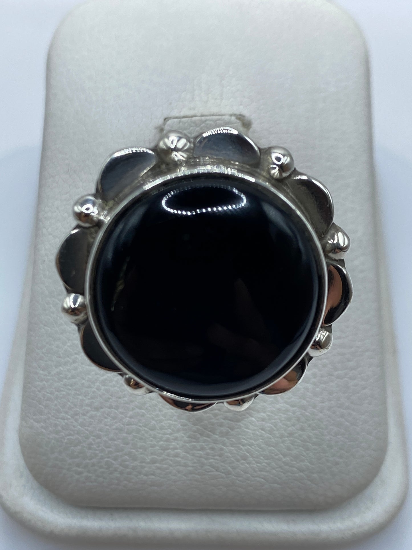 Anillo de plata con onix negro y flores en relieve, visto desde arriba sobre fondo blanco
