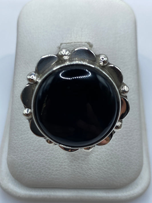 Anillo de plata con onix negro y flores en relieve, visto desde arriba sobre fondo blanco