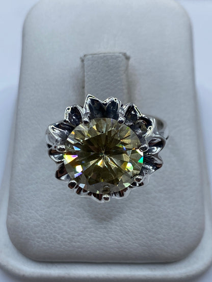 Anillo de plata .925 con circonia amarillo verdoso engastada en corona floral, visto de frente en estuche blanco