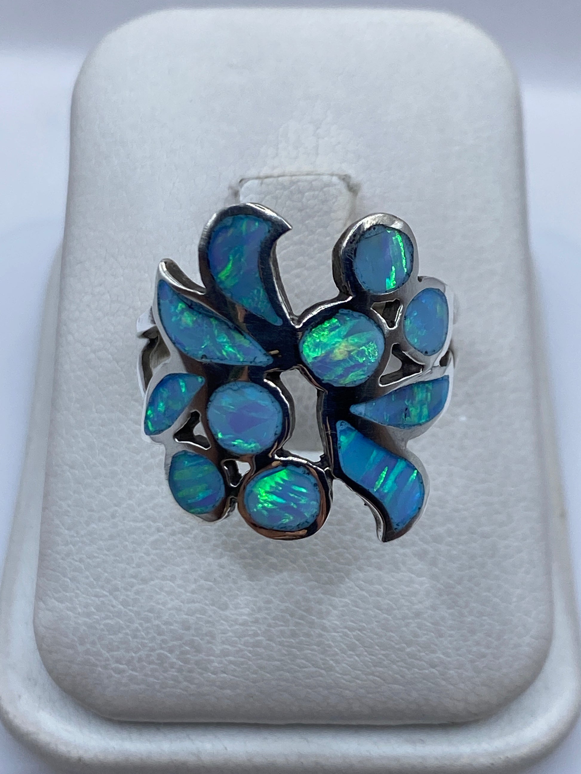 Anillo de plata con ópalo de fuego azul cielo iridiscente en diseño floral, sobre cojín blanco