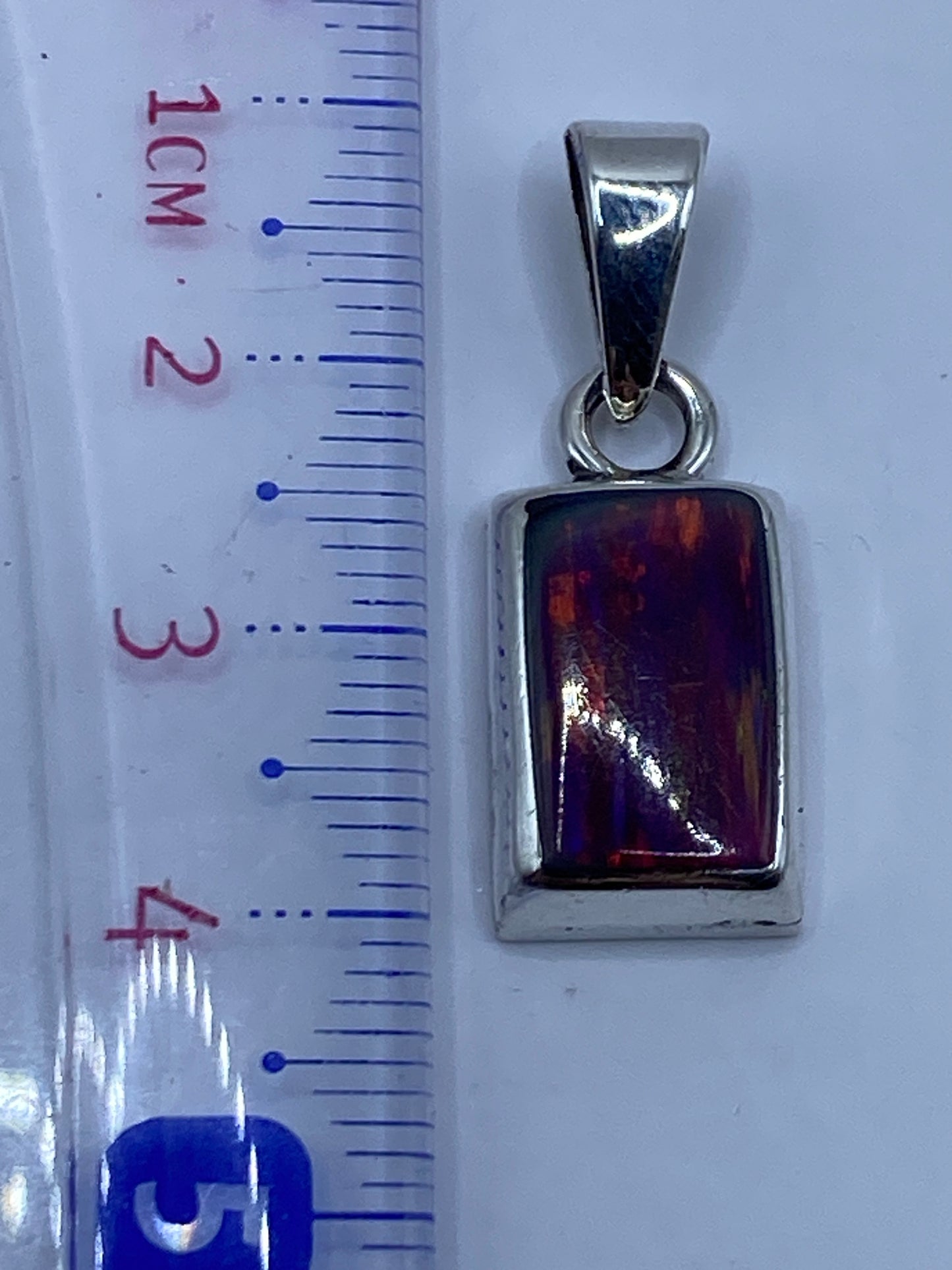 Dije de 3.8 cm junto a regla para referencia de tamaño, mostrando la piedra y engaste a mano