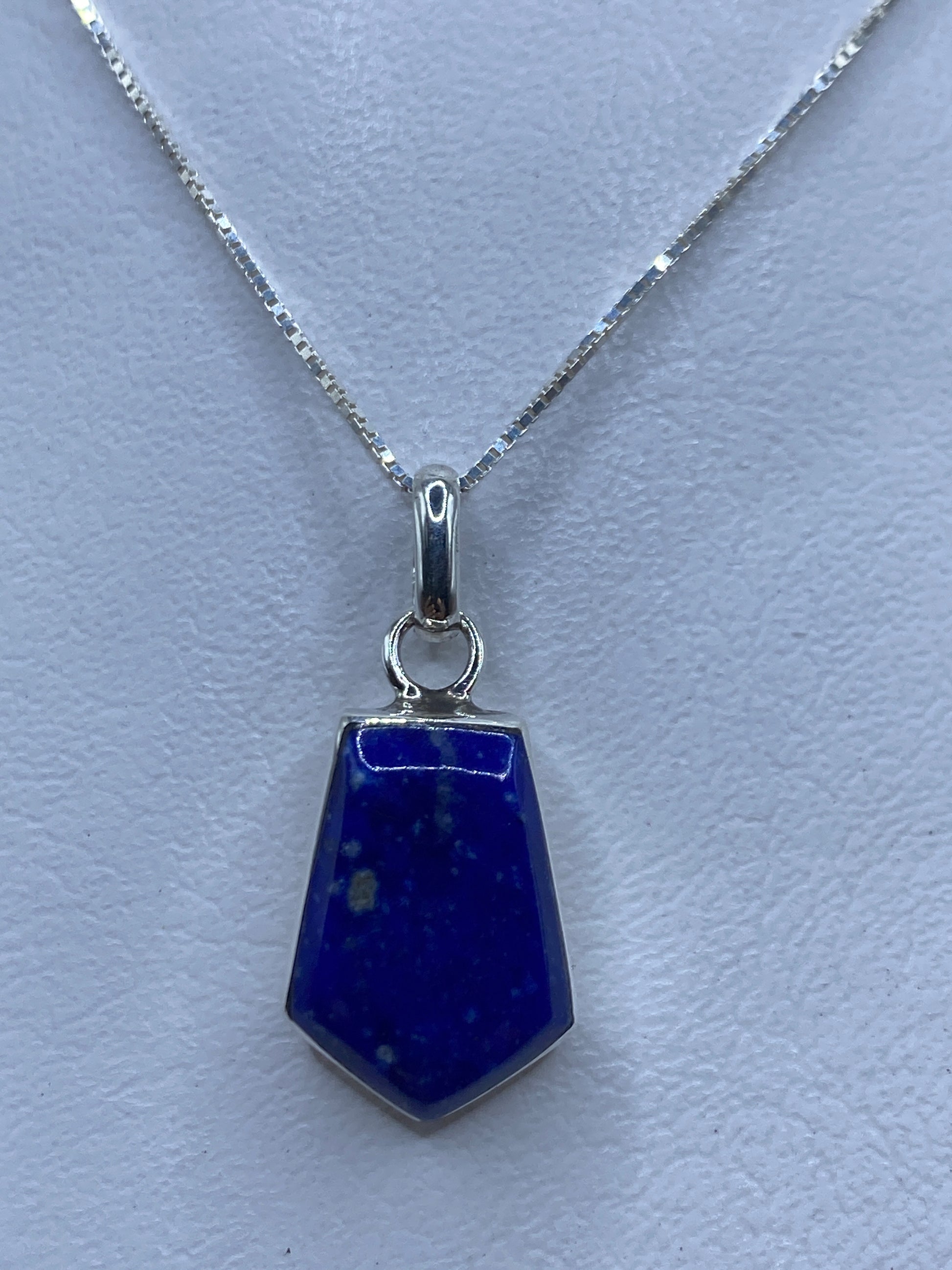 Dije de plata con piedra azul engastada, colgante sobre cadena delicada