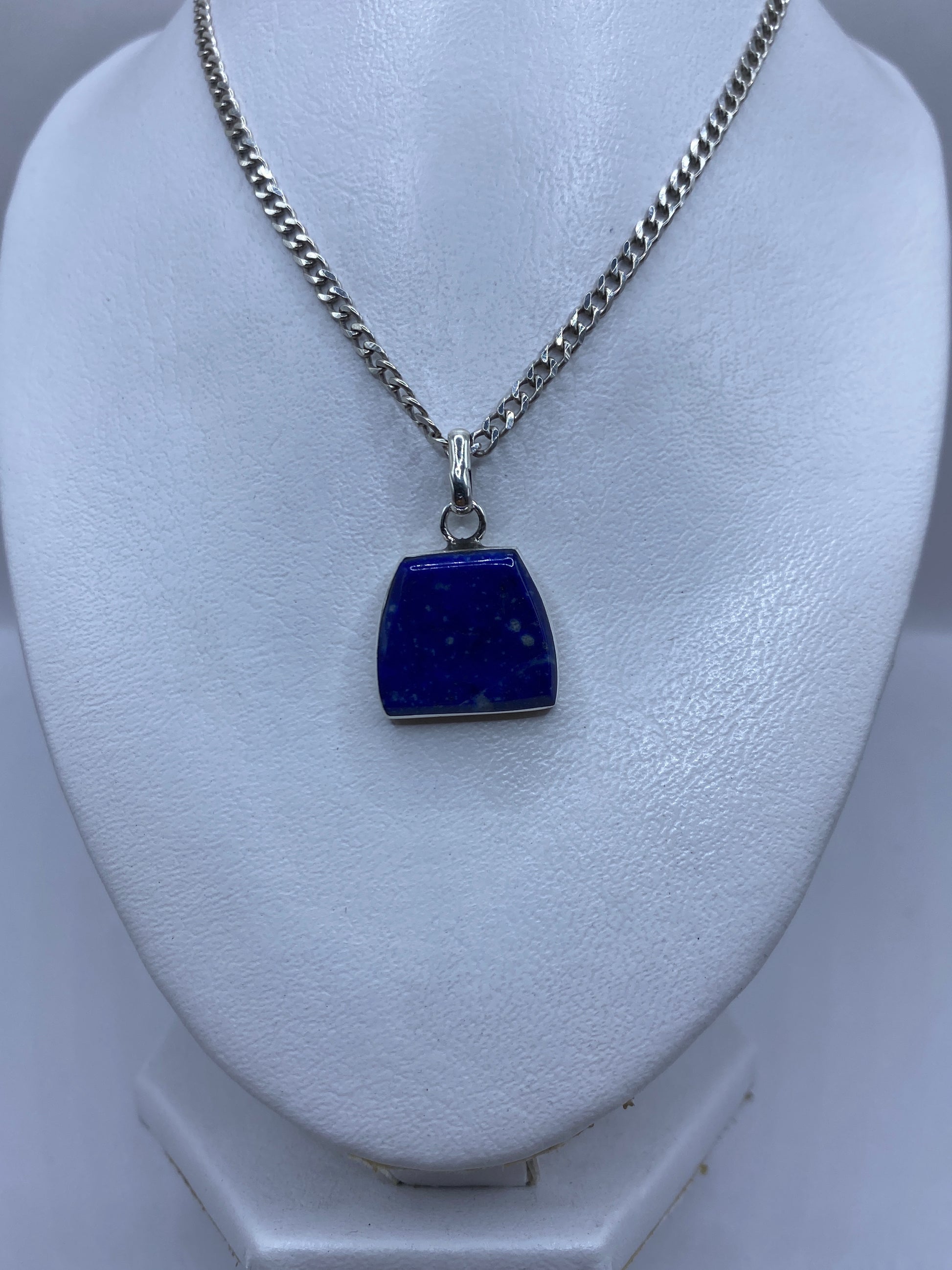 Dije de piedra azul engastada en plata, vista frontal sobre busto blanco