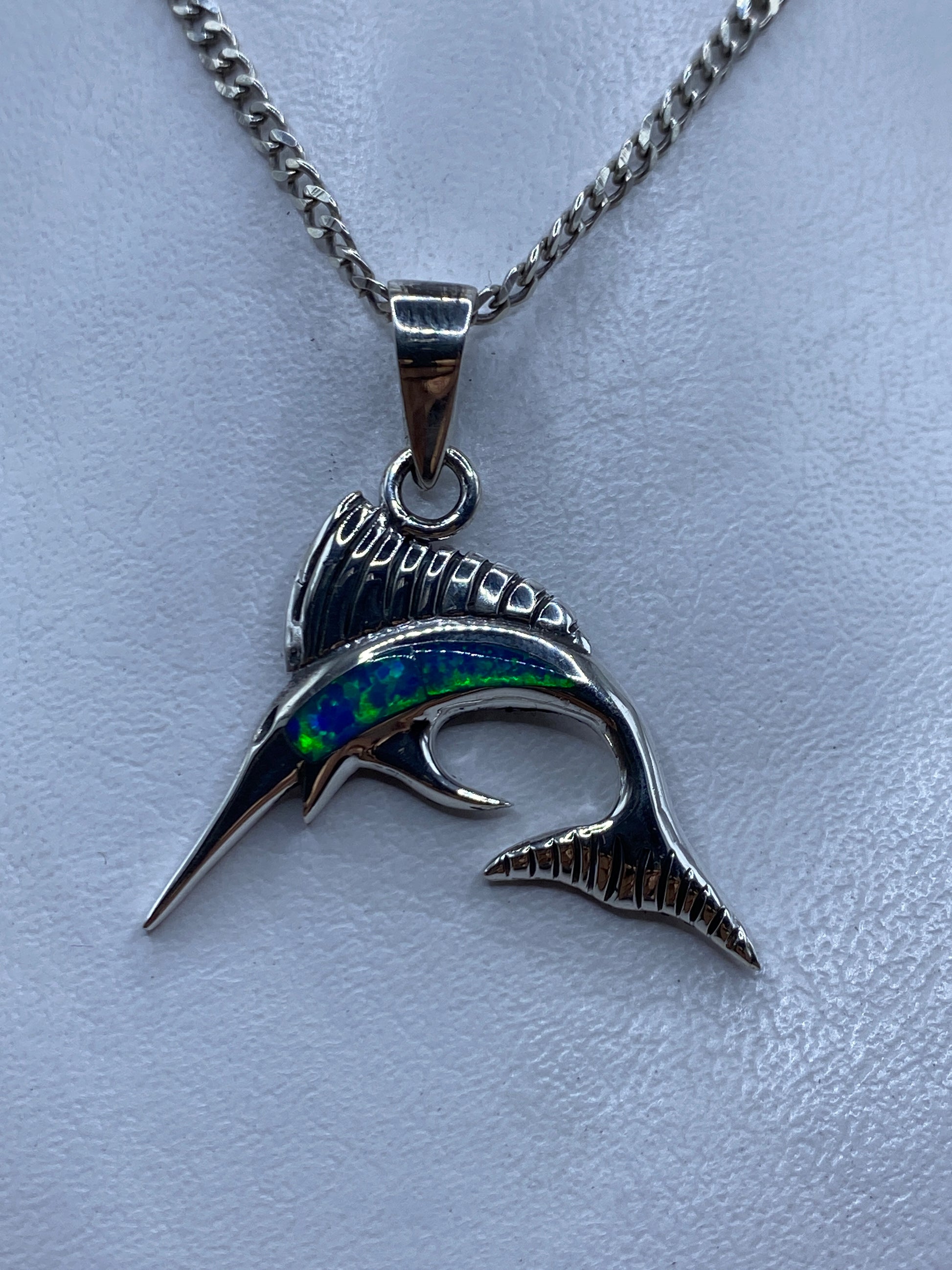 Dije de plata .950 con forma de marlin y opalo de fuego azul, colgando de cadena en el pecho