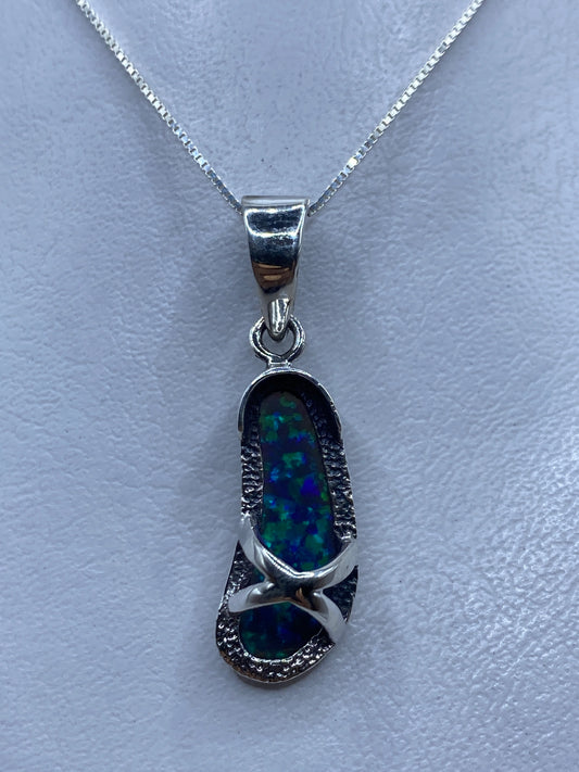 Dije de plata con ópalo de fuego azul, colgando de cadena plateada sobre fondo claro