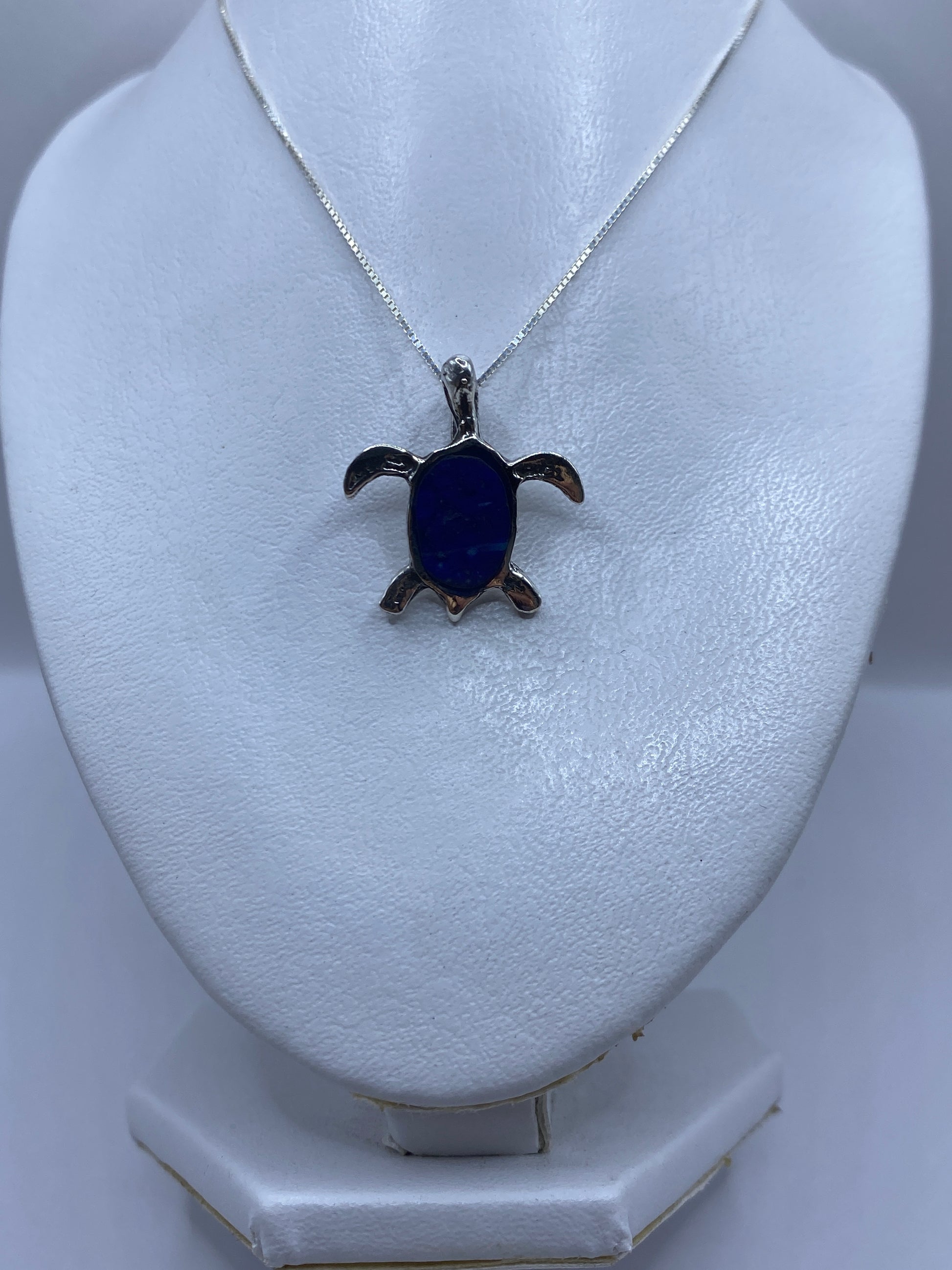 Detalle frontal del dije tortuga mostrando la piedra azul en el caparazón