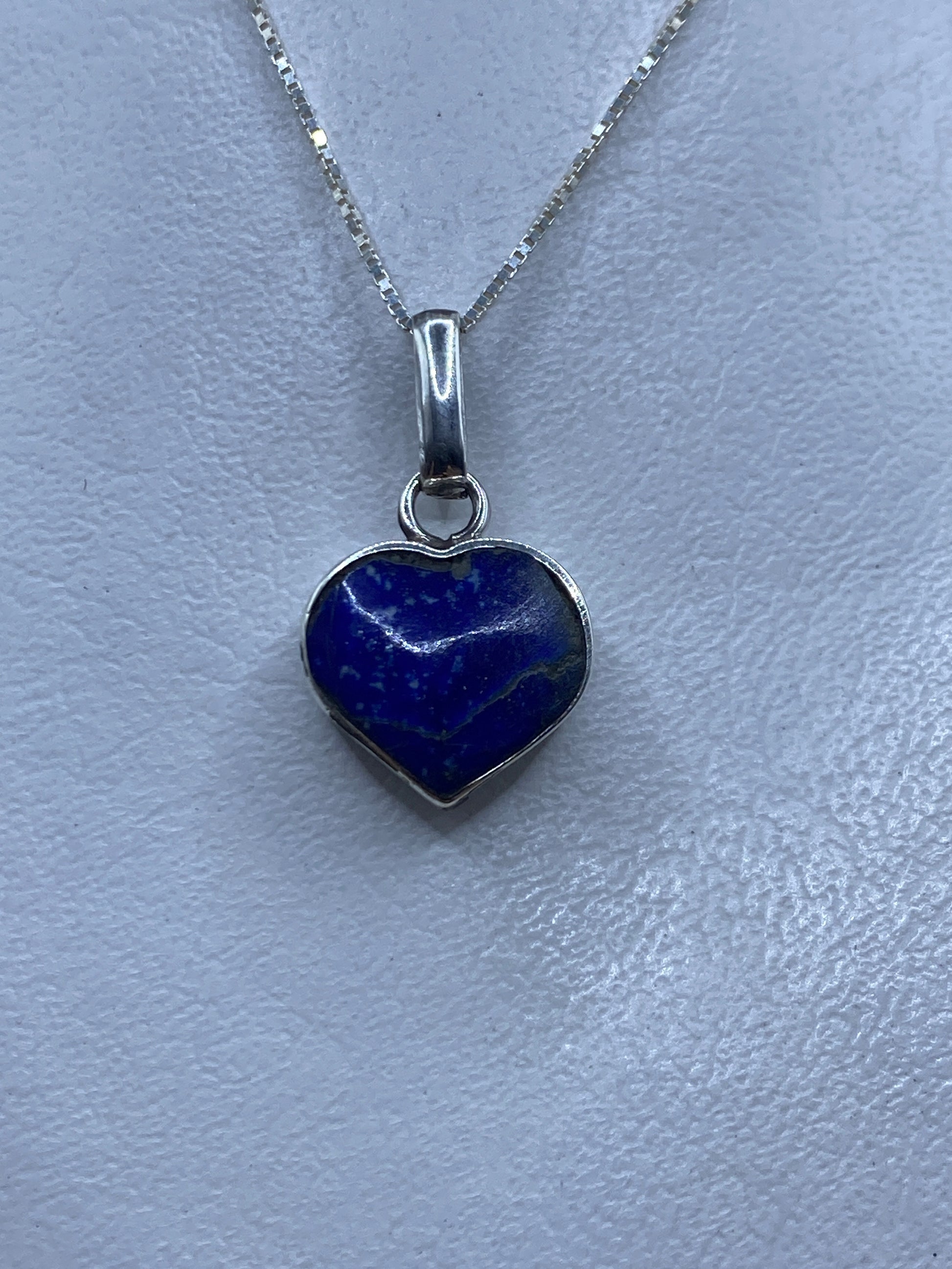 Dije de plata en forma de corazón con malaquita verde, colgado en cadena de plata sobre fondo gris claro