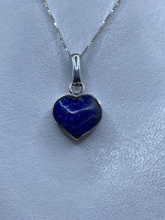 Dije de plata en forma de corazón con malaquita verde, colgado en cadena de plata sobre fondo gris claro