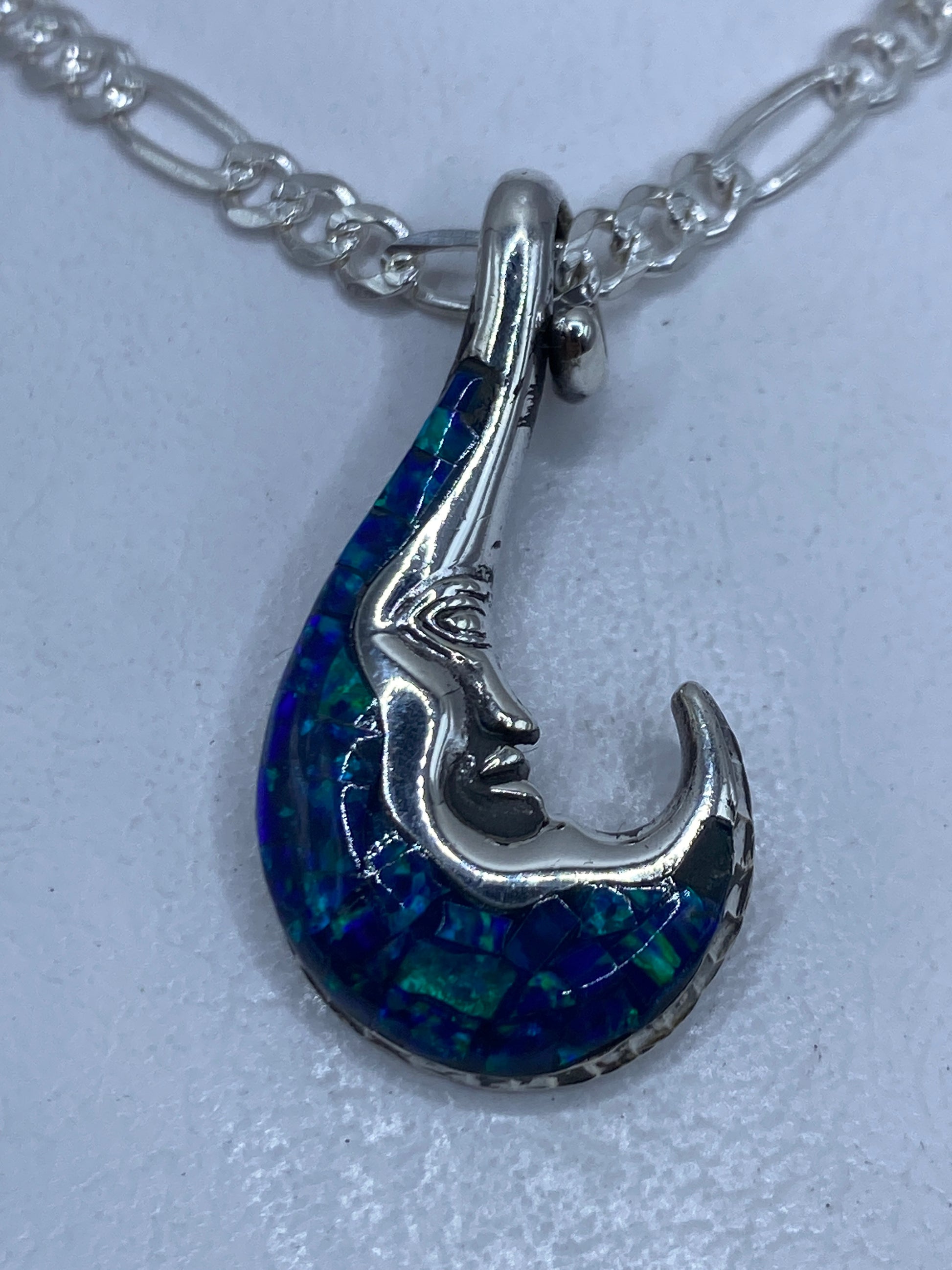 Dije de plata con forma de luna incrustada en ópalo de fuego azul, colgando de una cadena de plata