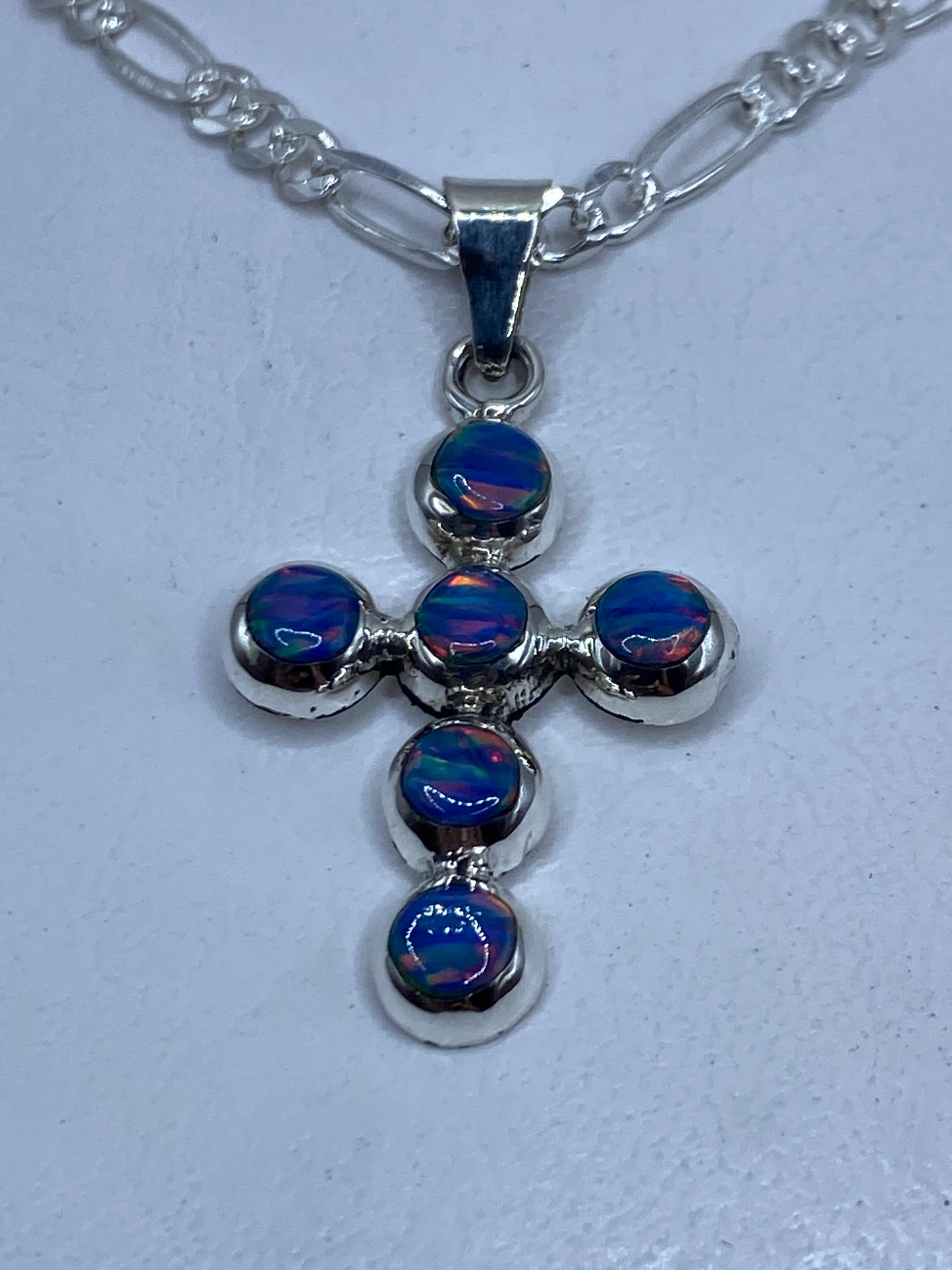 Cruz de plata .950 con ópalo de fuego azul sobre cadena plateada, vista frontal