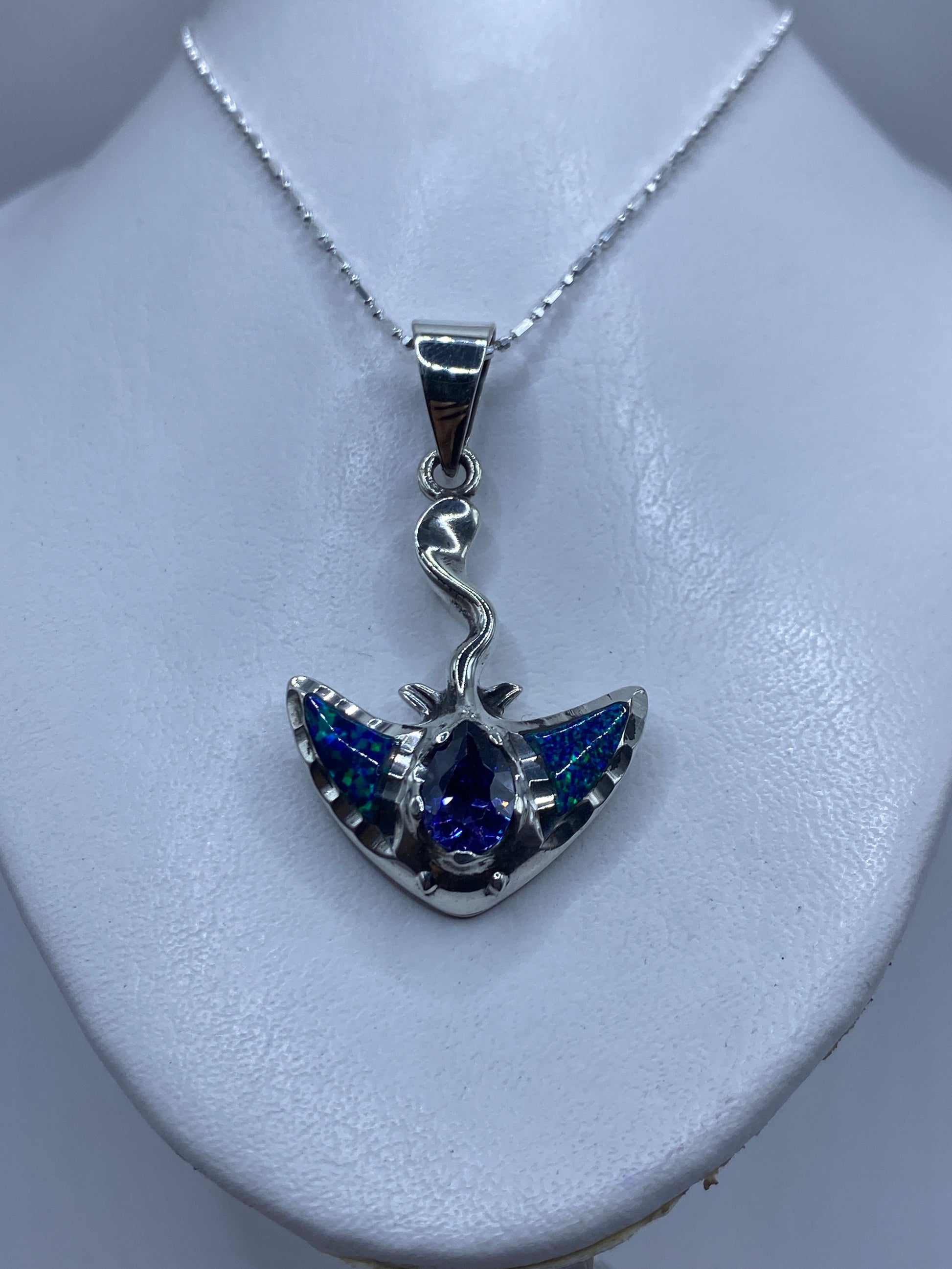 Detalle lateral del dije mostrando el engaste delicado de la piedra azul y las alas de plata