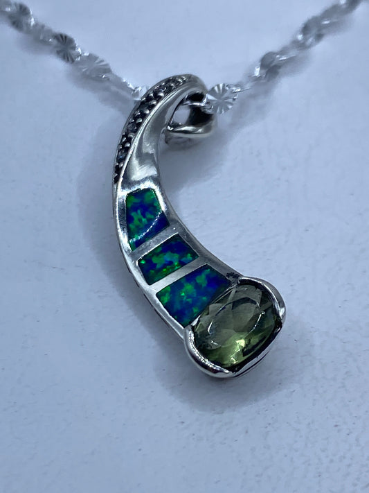Dije de plata .925 con ópalo de fuego engastado, tonos azul verdoso, colgando de cadena de plata