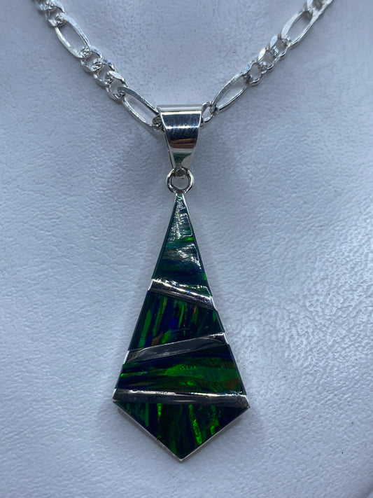 Dije tetraédrico de plata .950 con ópalo de fuego verde sobre cadena figaro en la piel