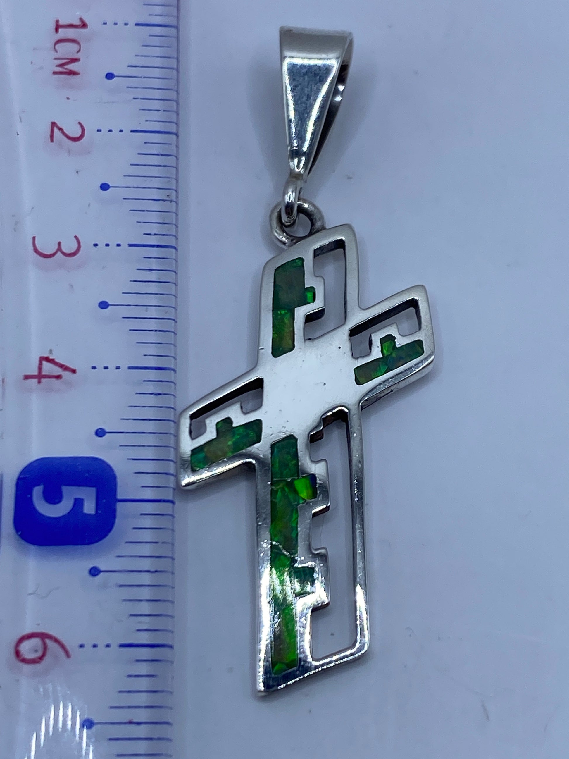 Dije cruz de 6 cm sobre escala de centímetros, mostrando el tamaño real con el ópalo verde limón