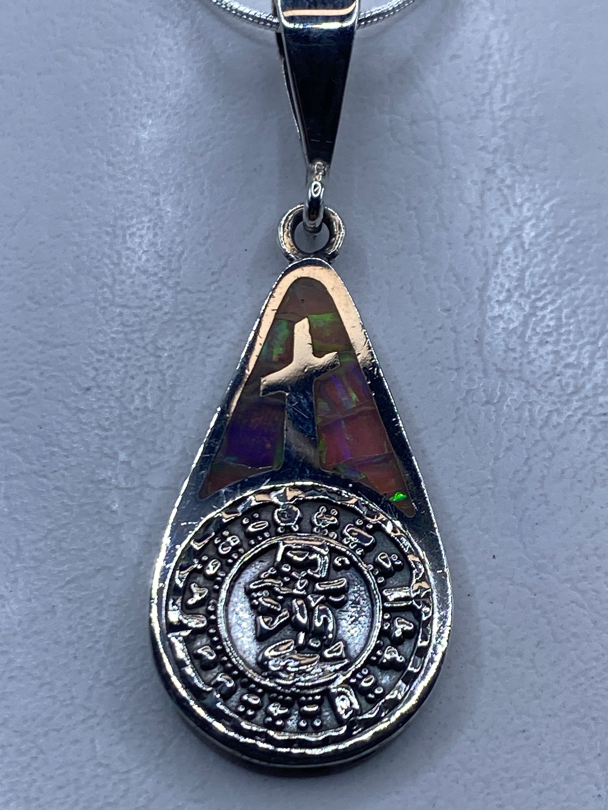 Dije cruz de plata .950 con opalo de fuego multicolor e inscripción zodiacal