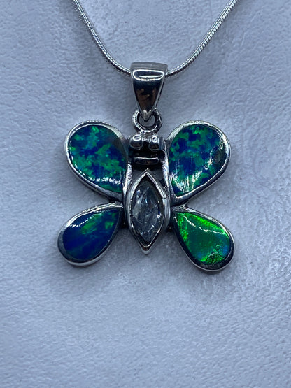 Dije mariposa de plata .925 con ópalo de fuego azul, engaste a mano, sobre fondo blanco