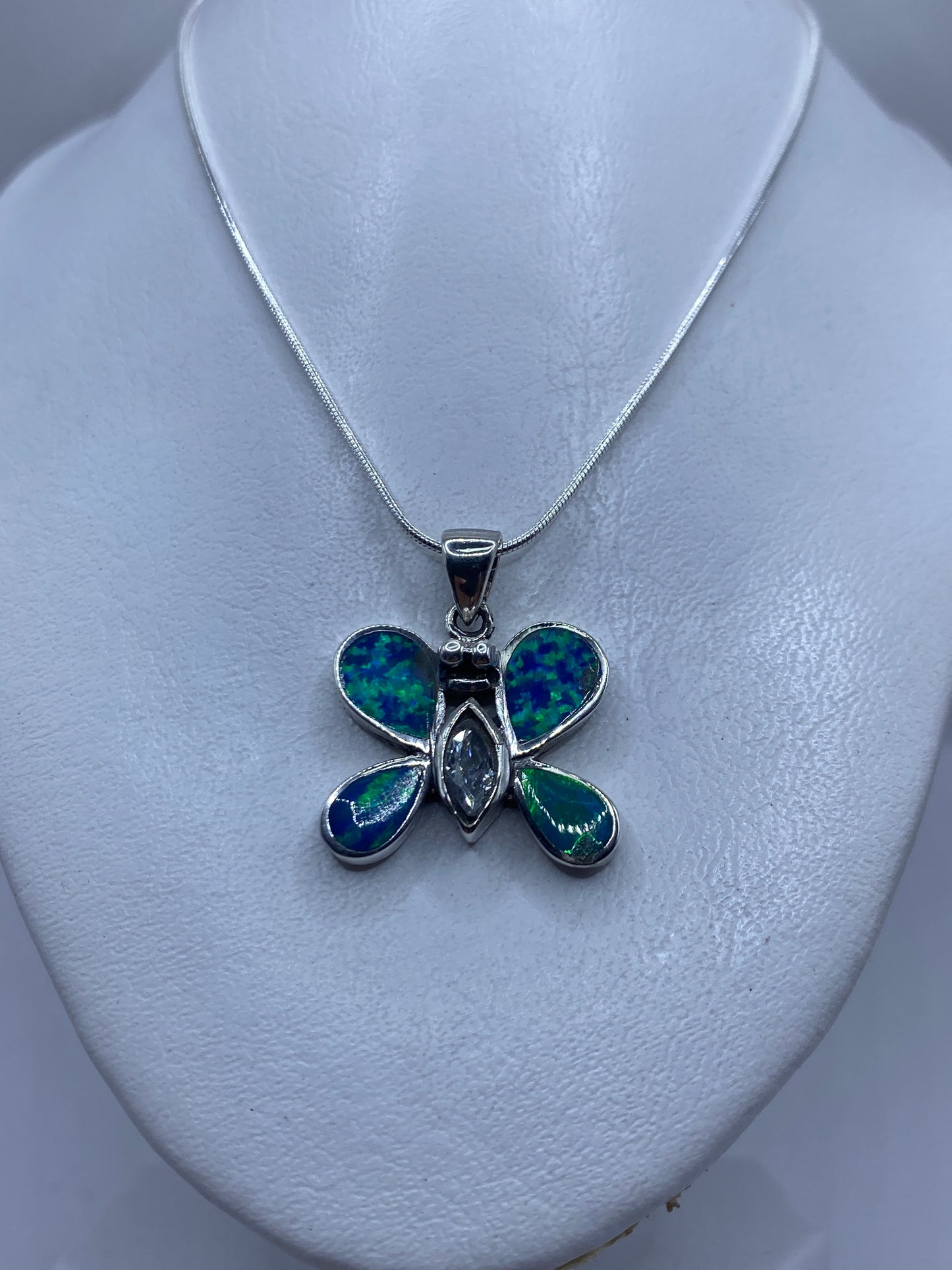Detalle del dije mariposa mostrando el juego de color azul y verde del ópalo de fuego