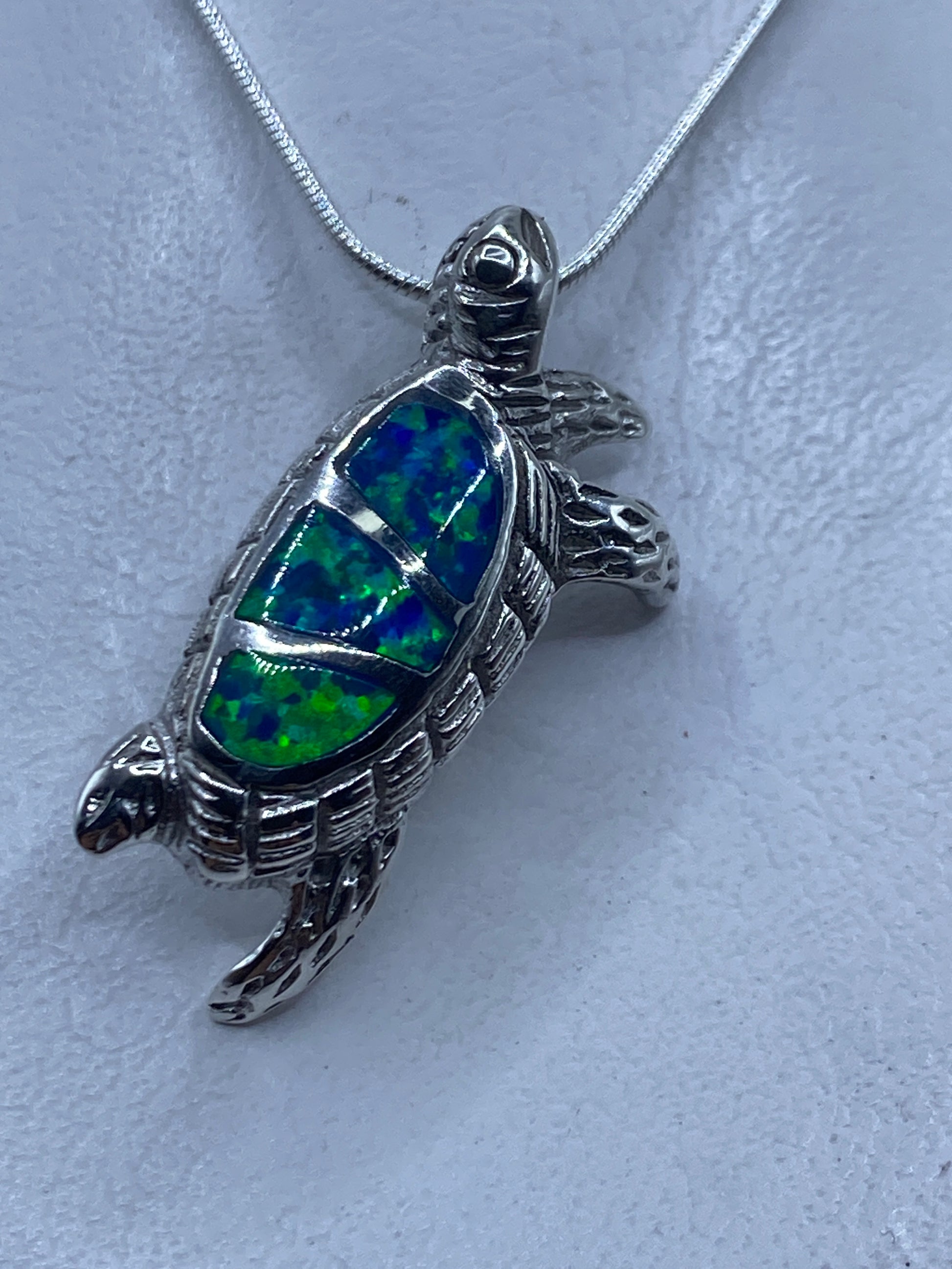 Dije tortuga de plata .925 con ópalo de fuego azul, colgando de cadena de eslabones finos