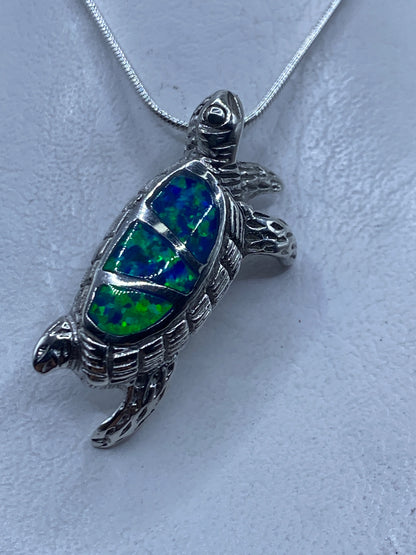 Dije tortuga de plata .925 con ópalo de fuego azul, colgando de cadena de eslabones finos