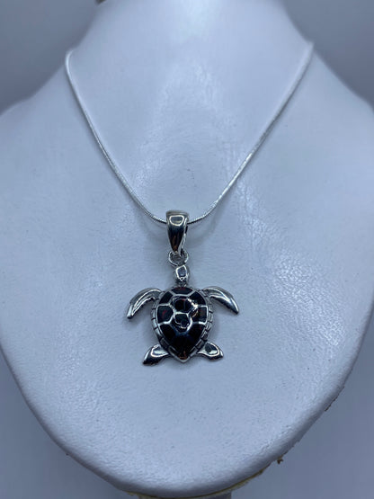 Dije de tortuga de 3.9 cm de largo mostrado junto a una regla para escala