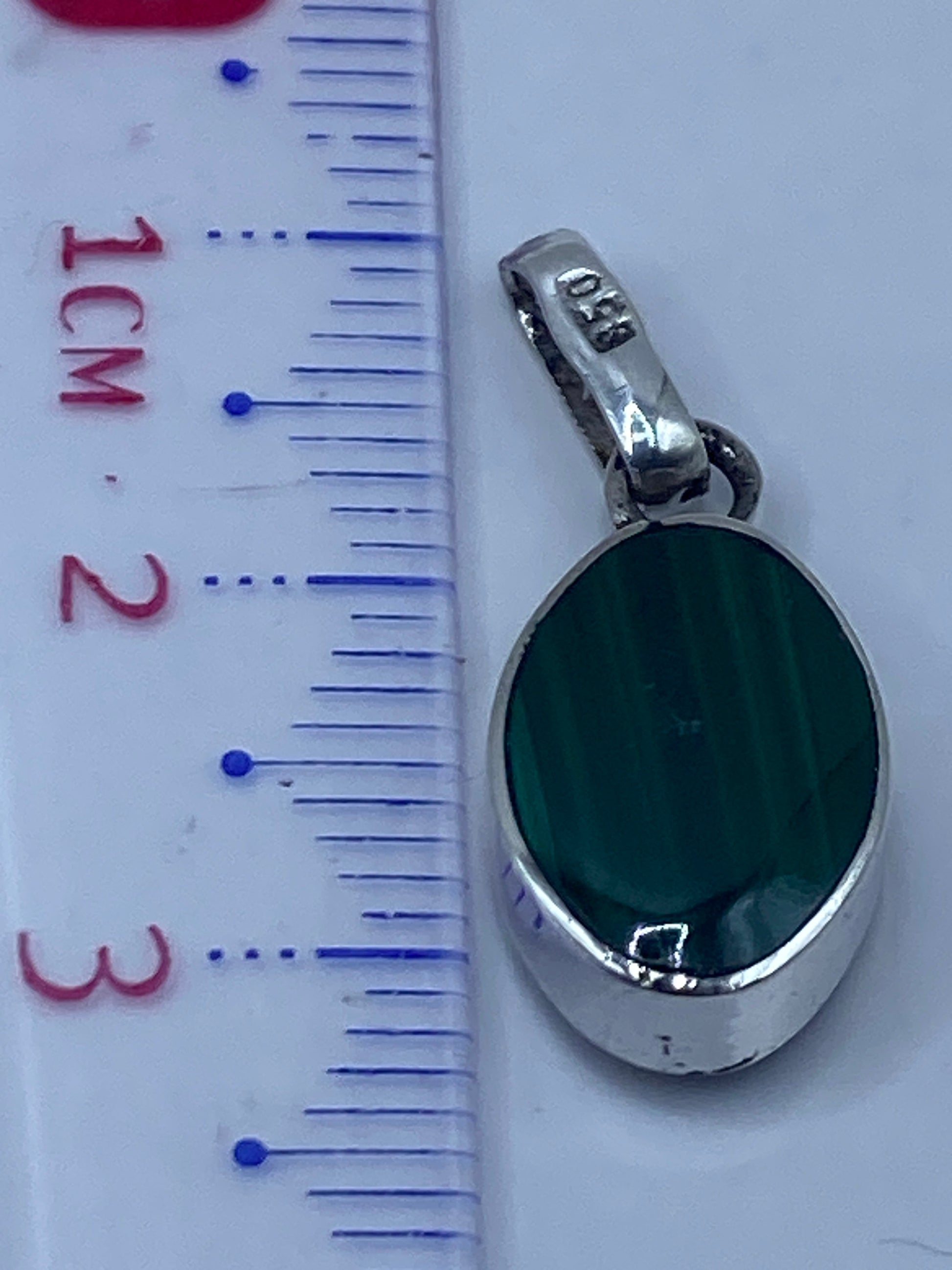 Escala de medición mostrando el dije de 3.3 cm de largo en comparación con una regla