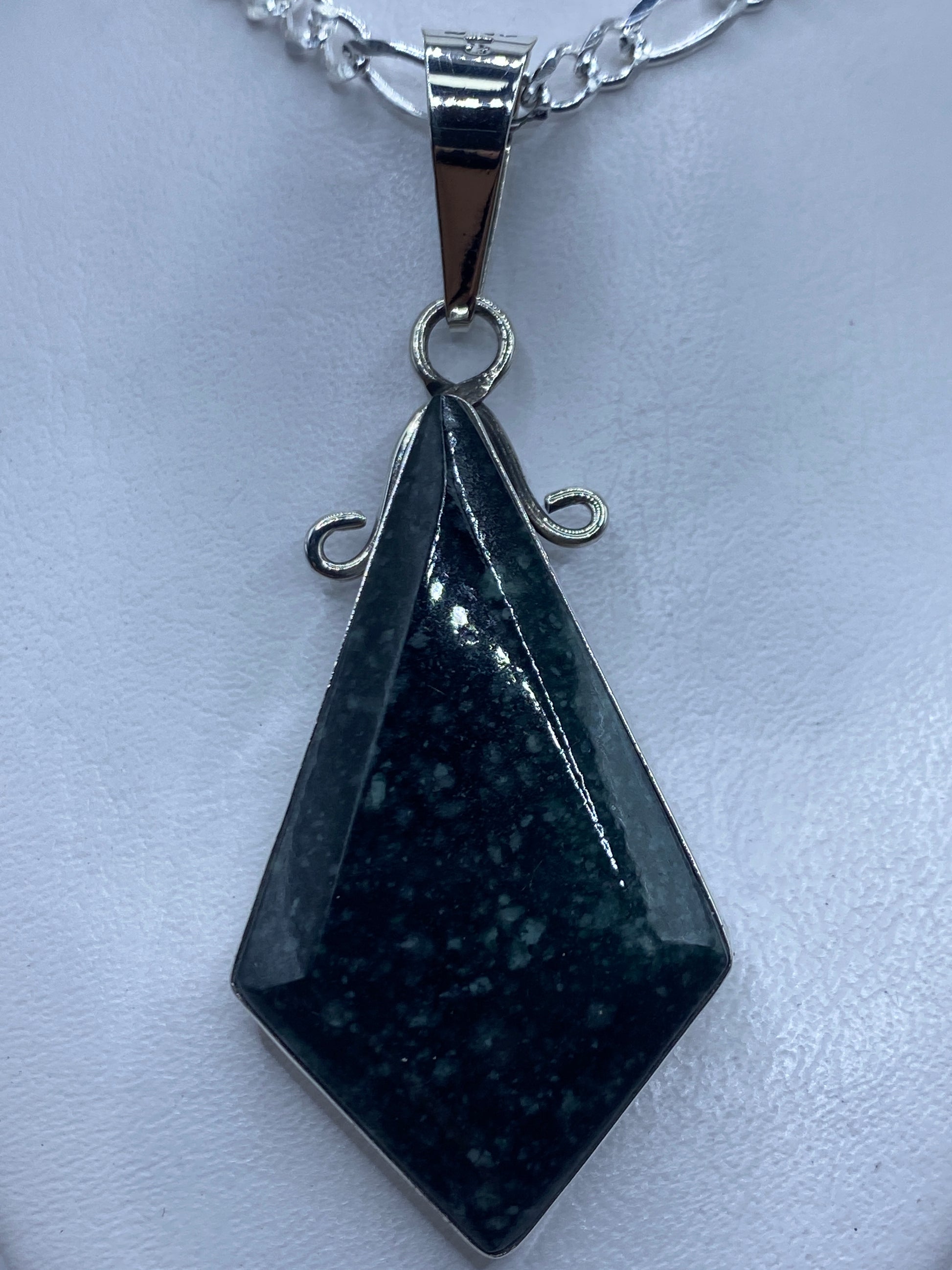 Dije de plata geométrico facetado con piedra, colgando de una cadena de plata brillante