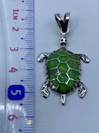 Dije de tortuga sobre fondo blanco con regla mostrando 5.3 cm de largo total